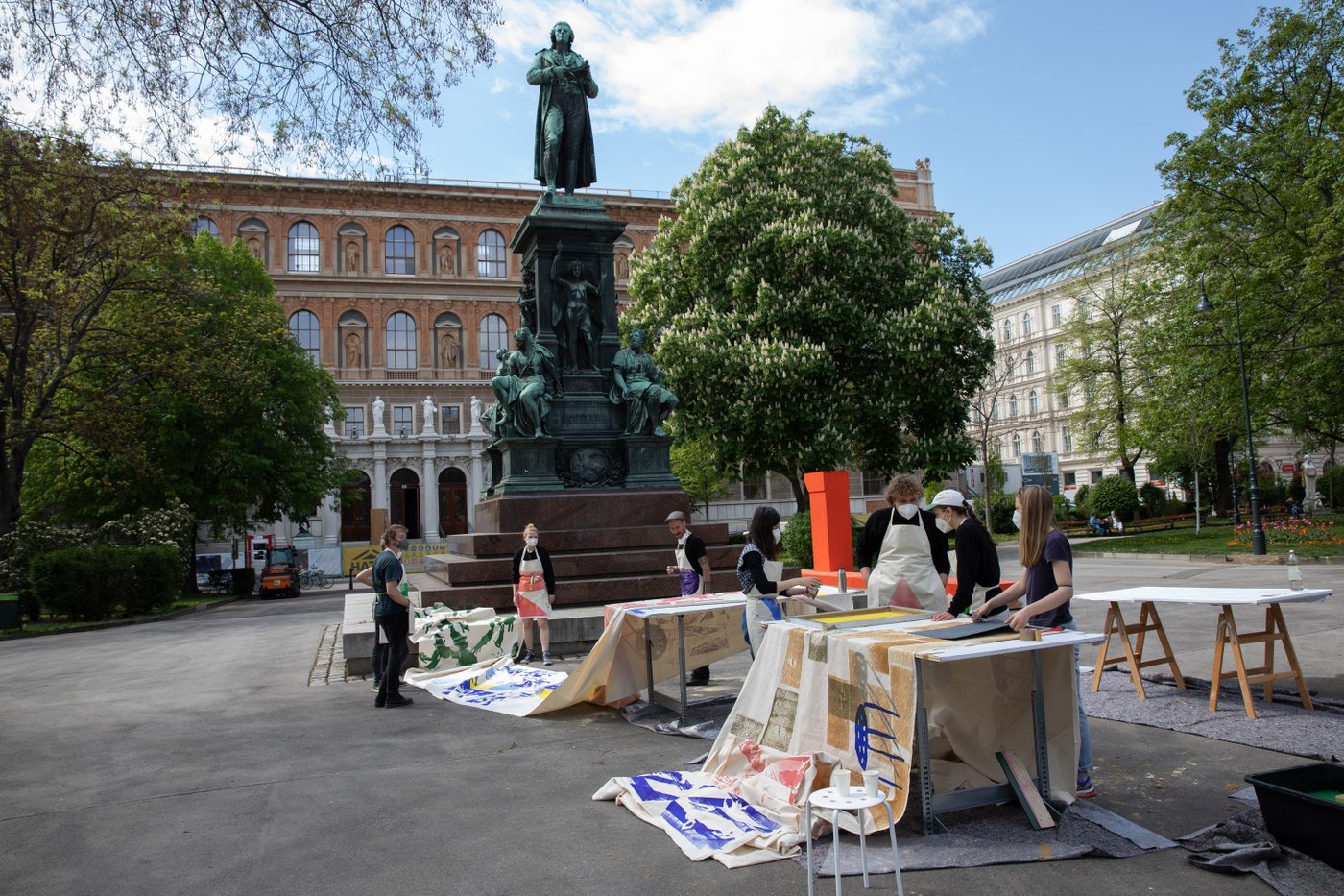 Students print on fabric in front of the Schiller monument. In the background you can see the academy building.