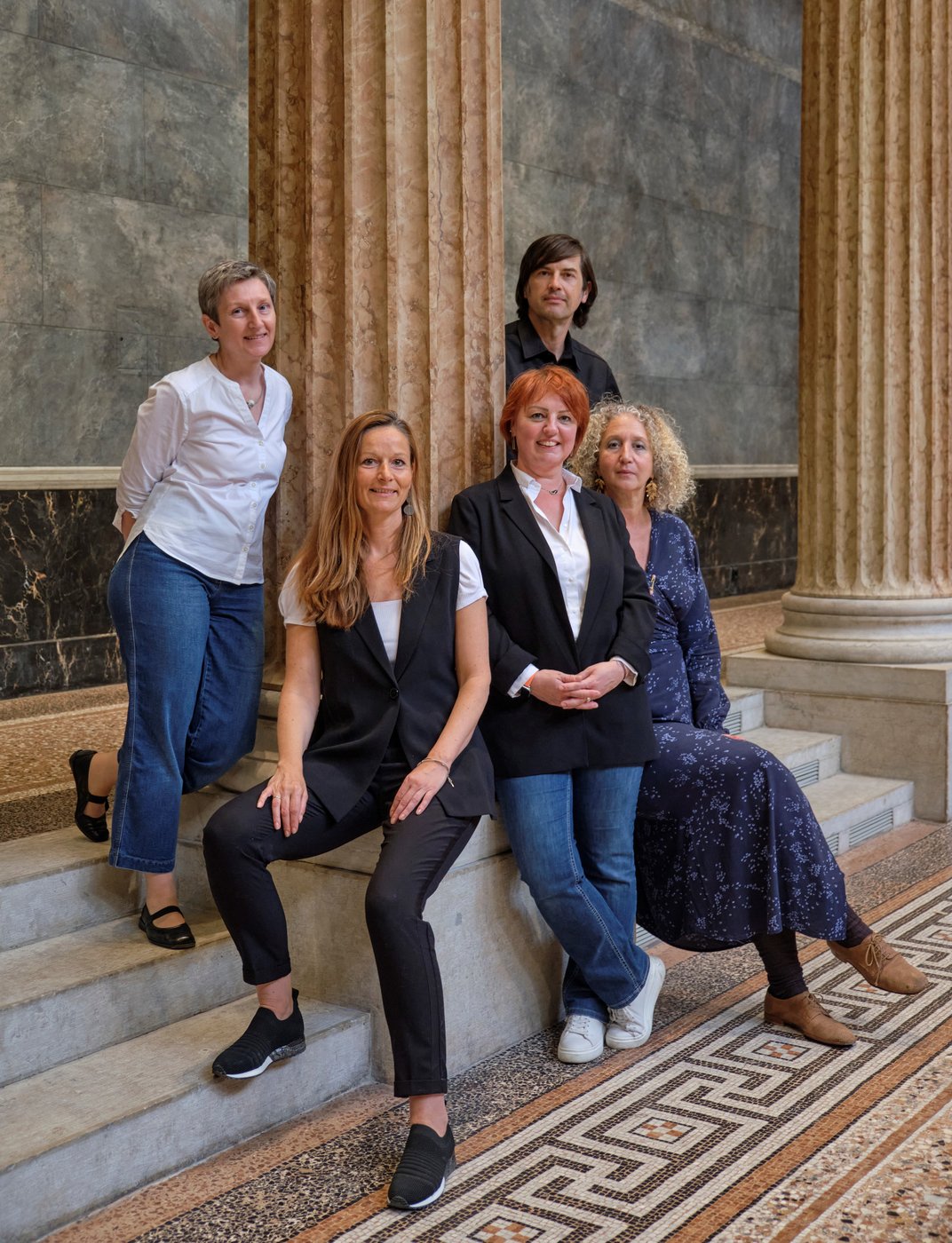 Picture of a group of people who are posing for a picture and some of them are leaning on a pillar.