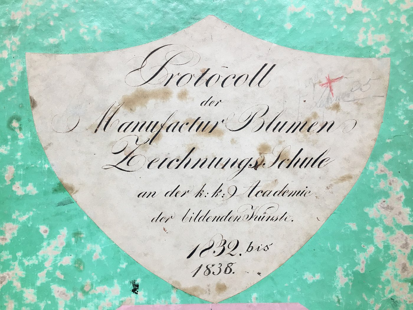 Detail of the cover of a matriculation book made of green paper, the paint has rubbed off in some places, pasted with a white label with the title and date of the book in ornate handwriting.