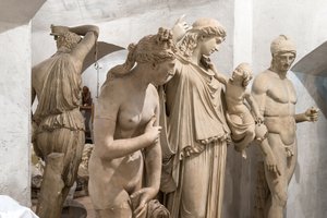 Three sculptures placed side by side in the white-washed vaulted basement of the Studiobuilding; due to the viewing angle, the leftmost figure, a cast of the ‘Capitoline Venus,’ appears to be the largest. The other two casts represent ‘Eirene carrying the infant Plutos on her arm’ and ‘Ares Borghese.’ All three sculptures are visible from the head to about the knee.