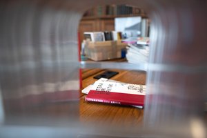 The color photograph shows a blurred wire frame through which a tunnel-like view of a table with books, stacked or in a box, is revealed.